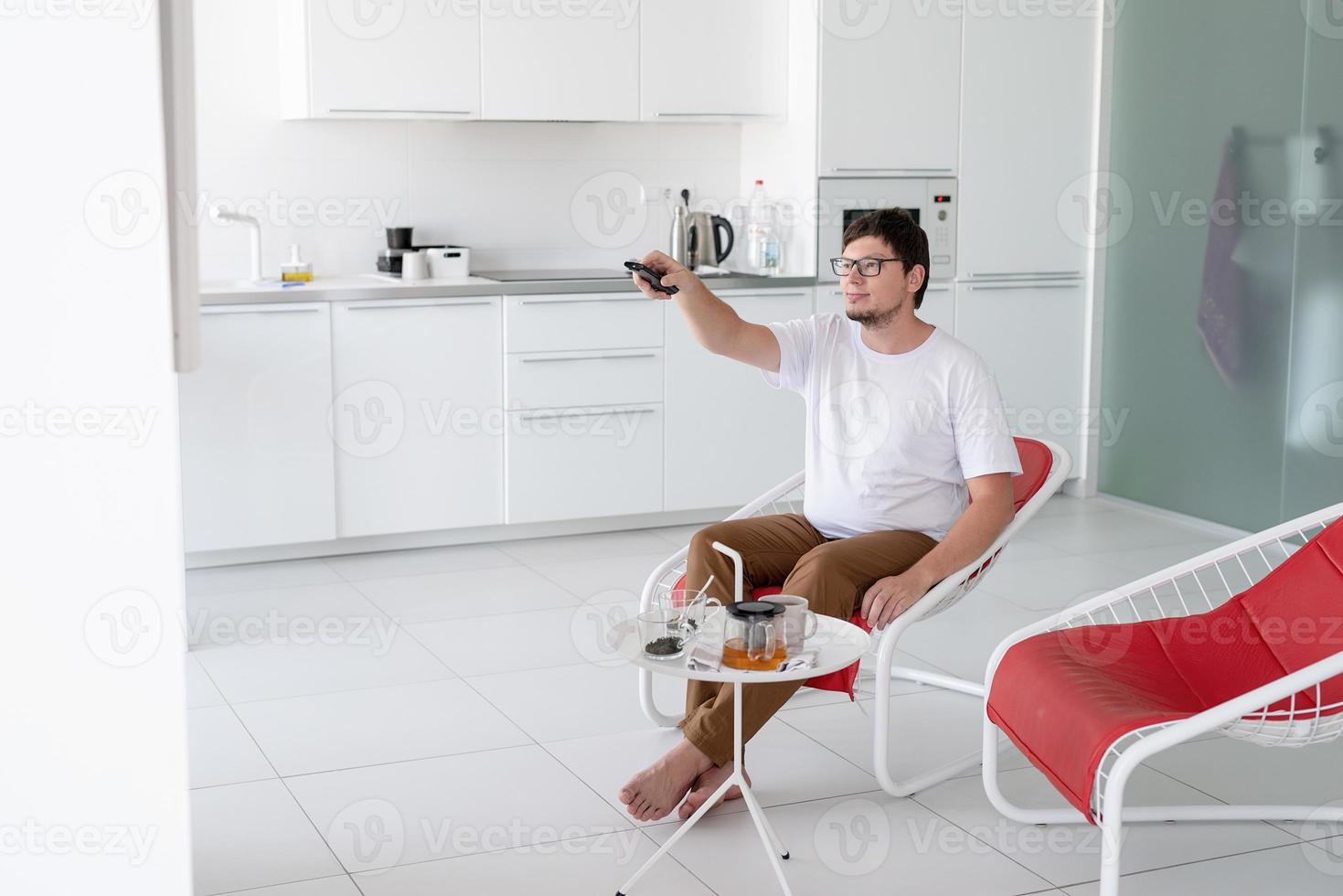 homem sentado em uma cadeira assistindo TV segurando o controle remoto foto