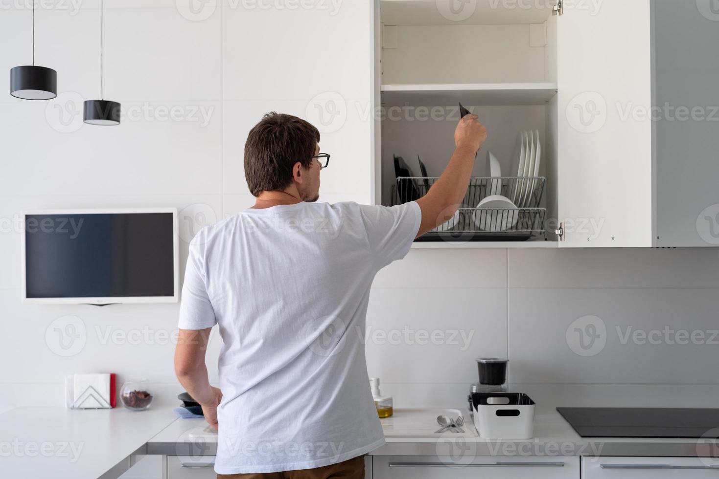homem de camiseta branca lavando pratos na cozinha foto