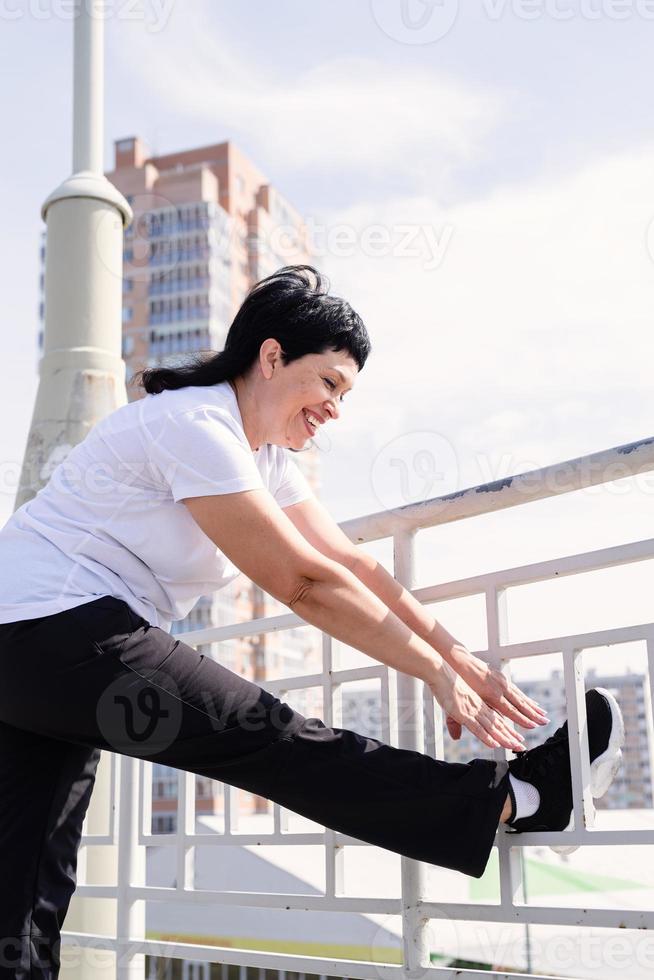 mulher sênior sorridente fazendo alongamento ao ar livre em meio urbano foto