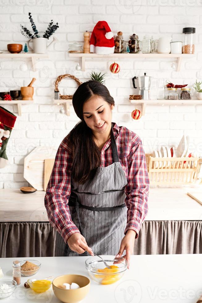 jovem latina mexendo ovos para cozinhar na cozinha foto