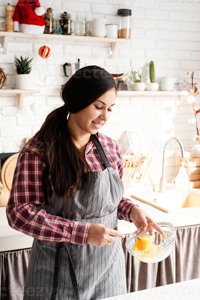 jovem latina mexendo ovos para cozinhar na cozinha foto