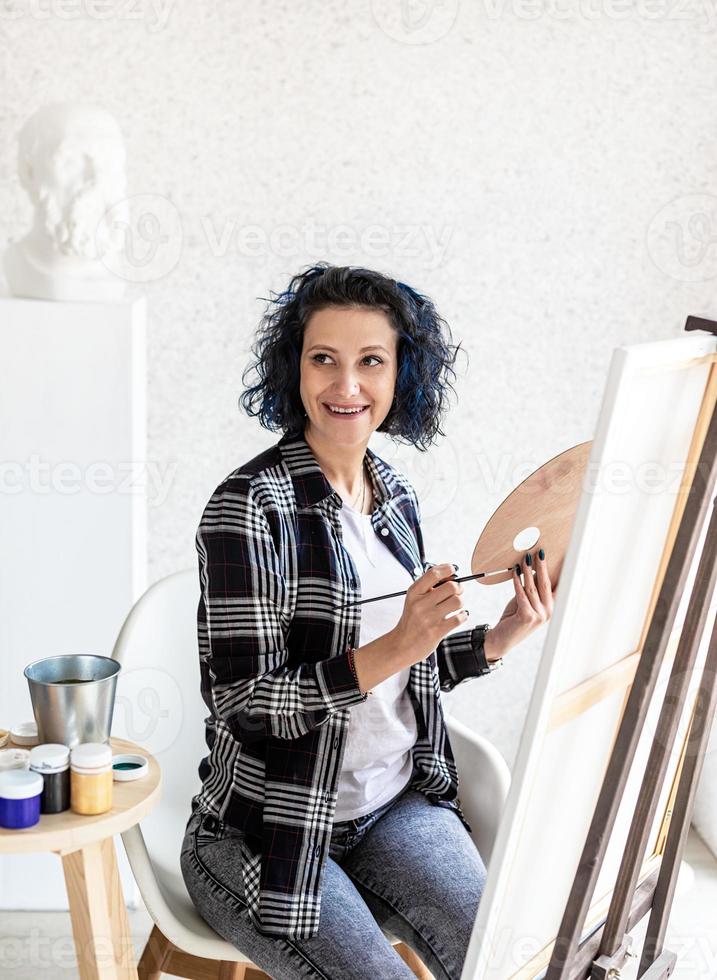 mulher criativa com cabelo tingido de azul pintando em seu estúdio foto