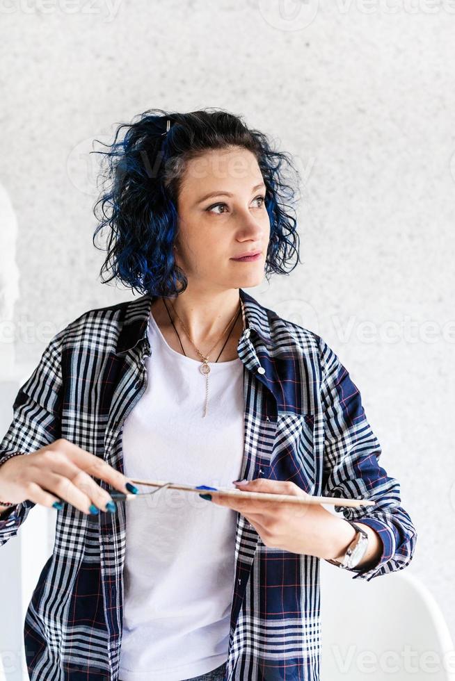 mulher criativa com cabelo tingido de azul pintando em seu estúdio foto