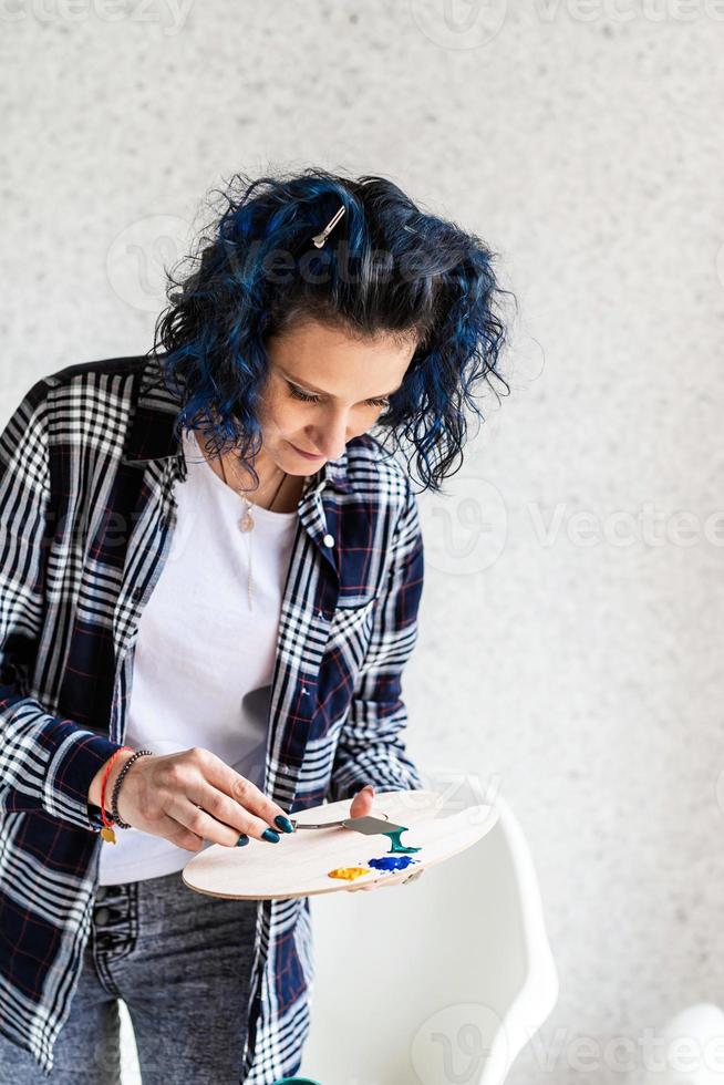 mulher criativa com cabelo tingido de azul pintando em seu estúdio foto