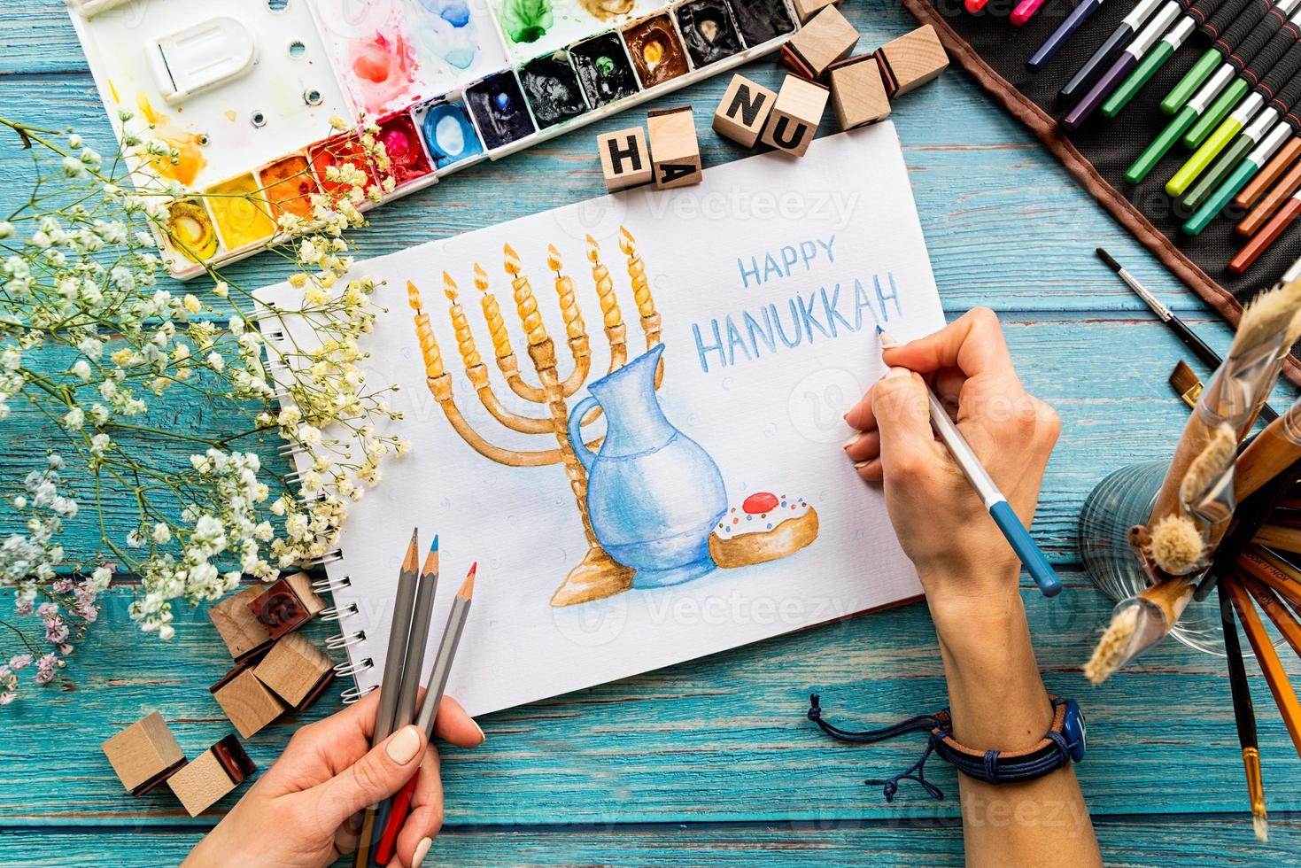 vista superior de mãos femininas desenhando uma arte em aquarela feliz hanukkah foto