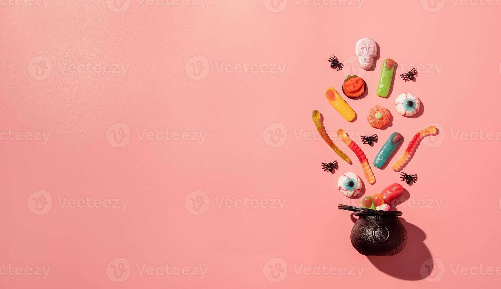 Doces de Halloween em um pote preto, vista superior em fundo rosa sólido foto