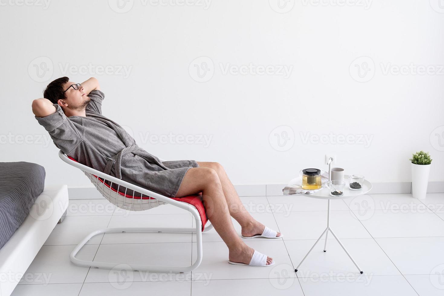 homem sentado em um roupão de banho fazendo chá em casa foto