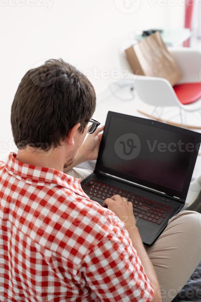 vista traseira de homem comprando na internet com laptop, tela preta foto