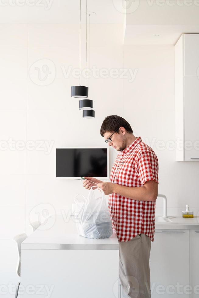 homem segurando um saco plástico descartável com entrega de comida na cozinha foto