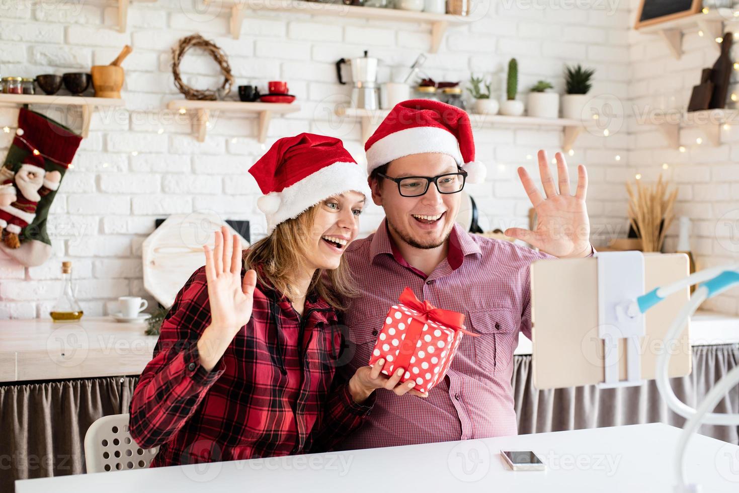 casal com chapéu de Papai Noel cumprimentando seus amigos em uma videochamada no tablet foto