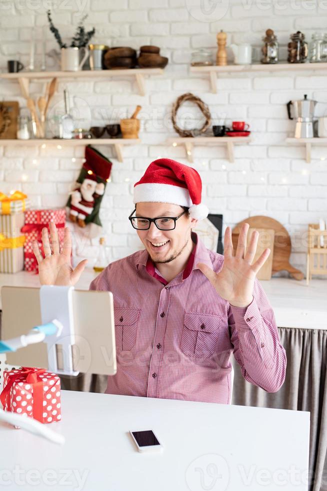 homem com chapéu de Papai Noel cumprimentando seus amigos em um bate-papo por vídeo ou uma ligação no tablet foto