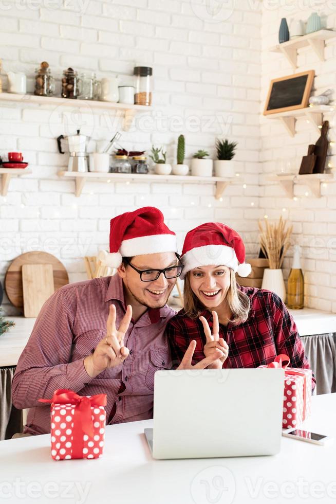 casal com chapéu de Papai Noel cumprimentando seus amigos em uma videochamada foto