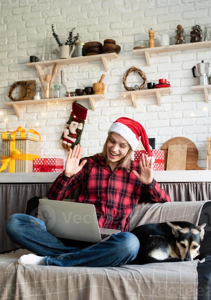 mulher com chapéu de Papai Noel cumprimentando seus amigos em chat por vídeo no laptop foto