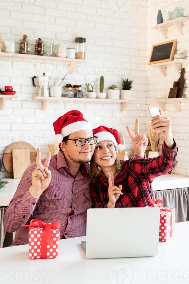 casal com chapéu de Papai Noel cumprimentando seus amigos em uma videochamada foto