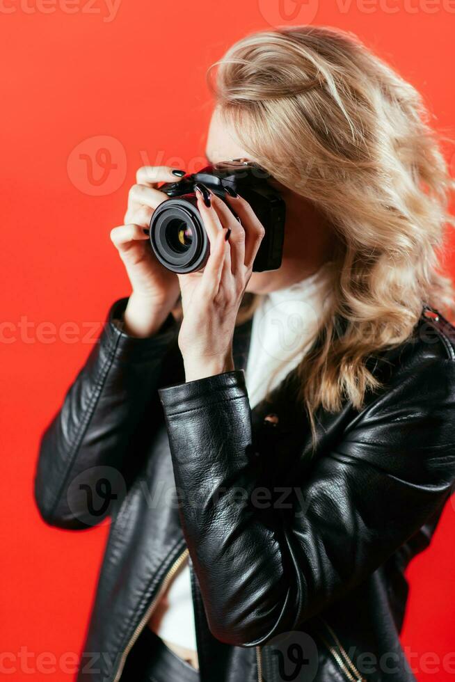 retrato do uma lindo menina fotógrafo com uma Câmera dentro dela mãos quem é fotografado dentro uma foto estúdio em uma vermelho fundo