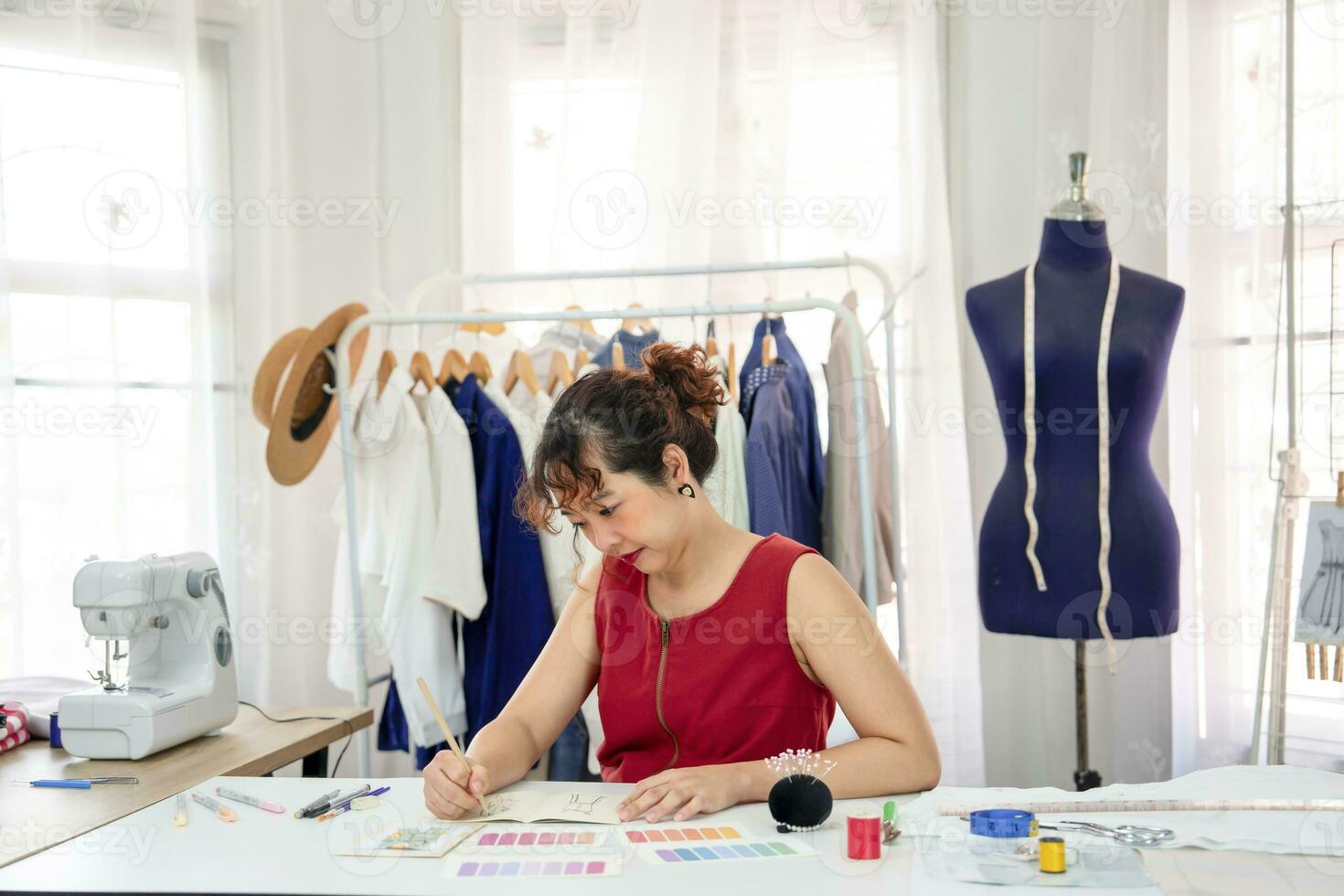 jovem ásia fêmea desenhador desenhando roupas Projeto em mesa, uma profissional costureira trabalhando dentro dela moderno moda estúdio. conceito roupas design, costura, alfaiataria, negócios, indústria foto