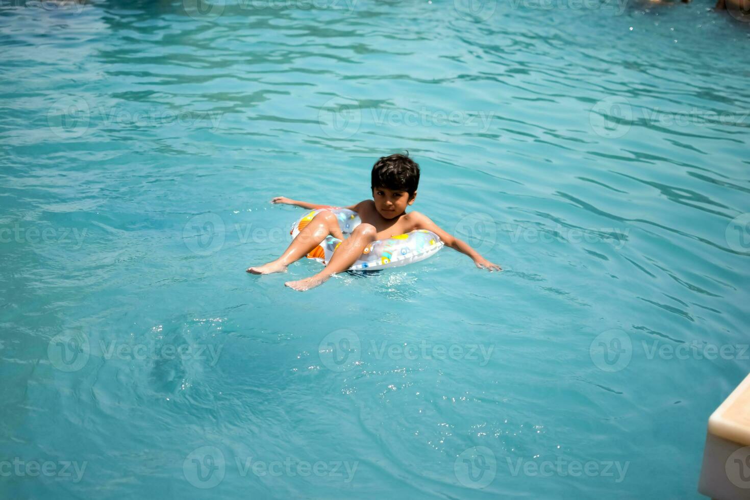 feliz indiano Garoto natação dentro uma piscina, criança vestindo natação traje ao longo com ar tubo durante quente verão Férias, crianças Garoto dentro grande natação piscina. foto