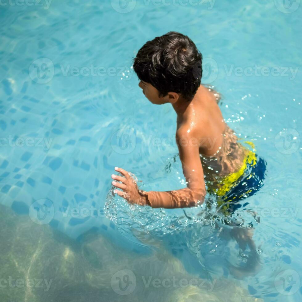 feliz indiano Garoto natação dentro uma piscina, criança vestindo natação traje ao longo com ar tubo durante quente verão Férias, crianças Garoto dentro grande natação piscina. foto