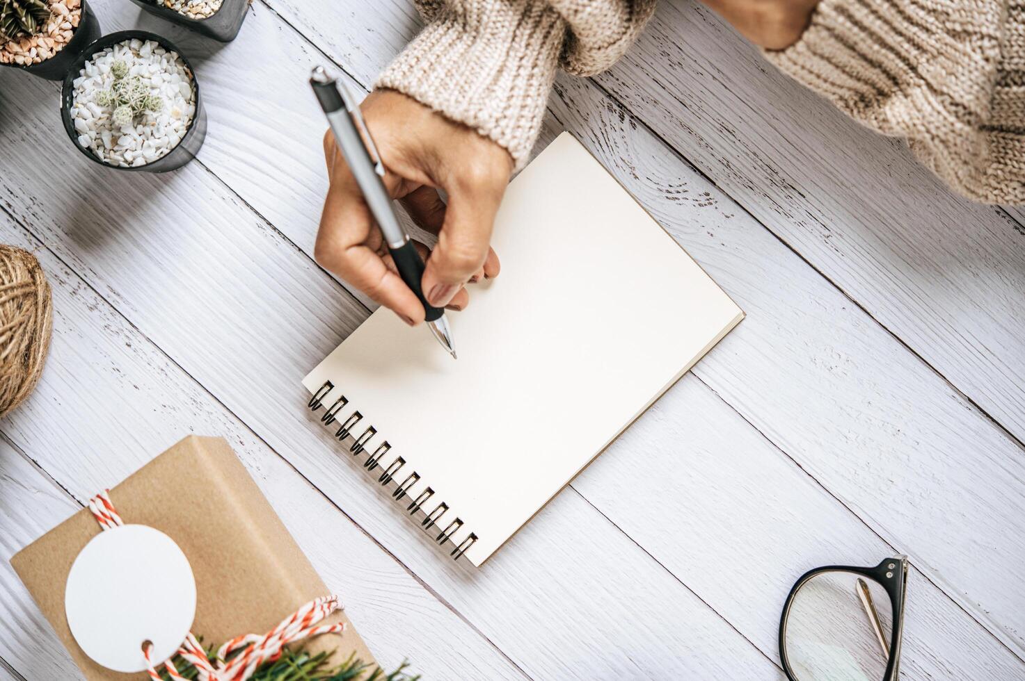 uma mão segurando uma caneta para escrever em um caderno com óculos foto