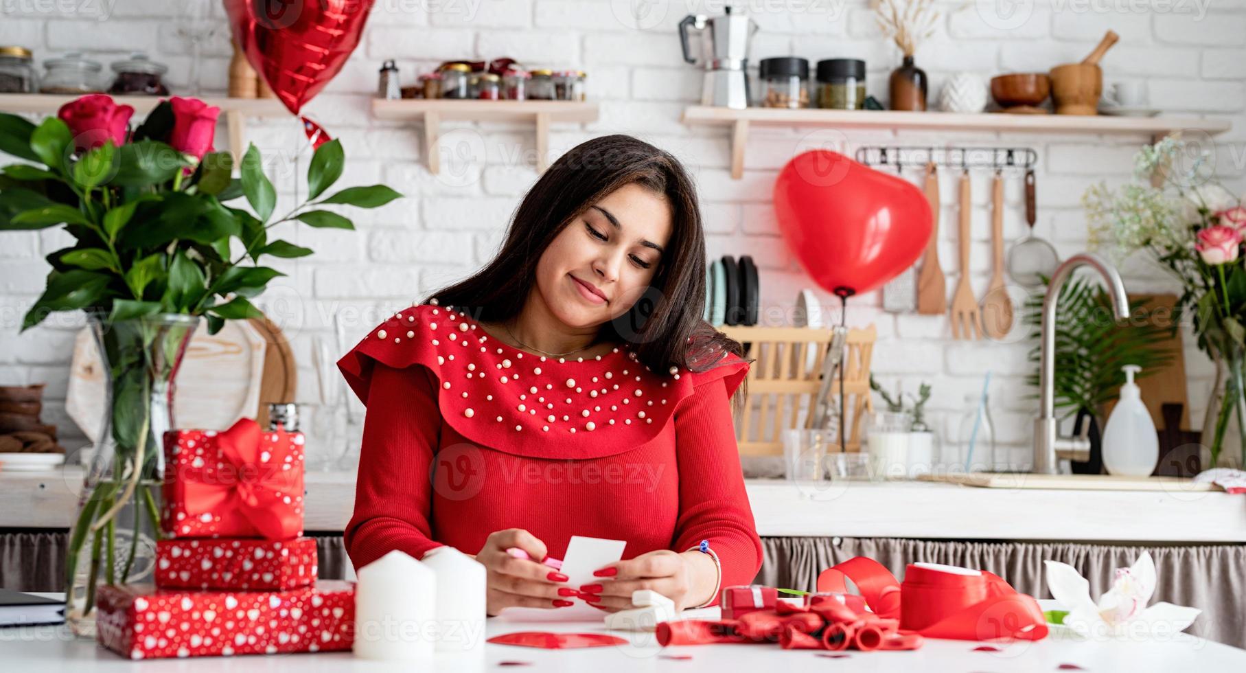 jovem escrevendo uma carta de amor sentada na cozinha decorada foto