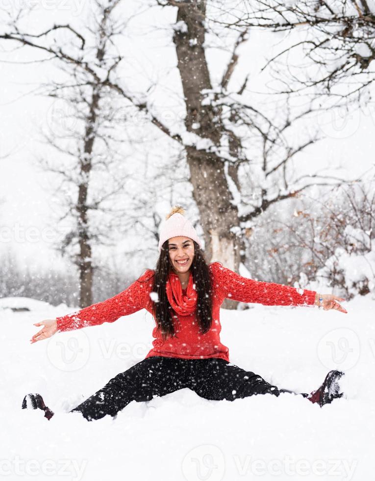 jovem morena de suéter vermelho brincando com a neve no parque foto