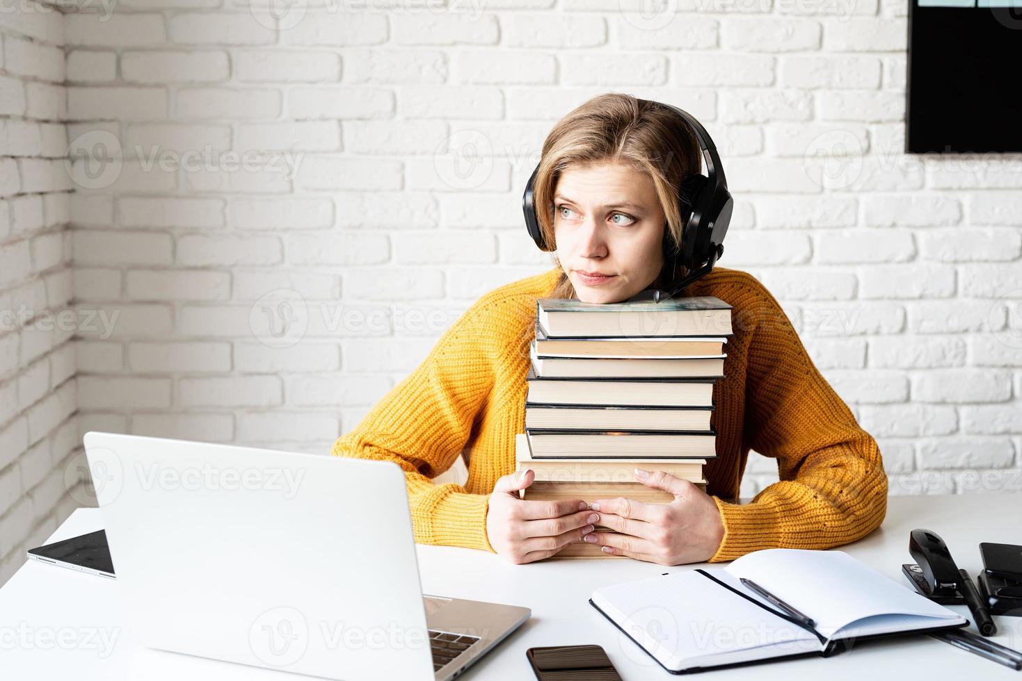 jovem estudando online segurando uma pilha de livros foto