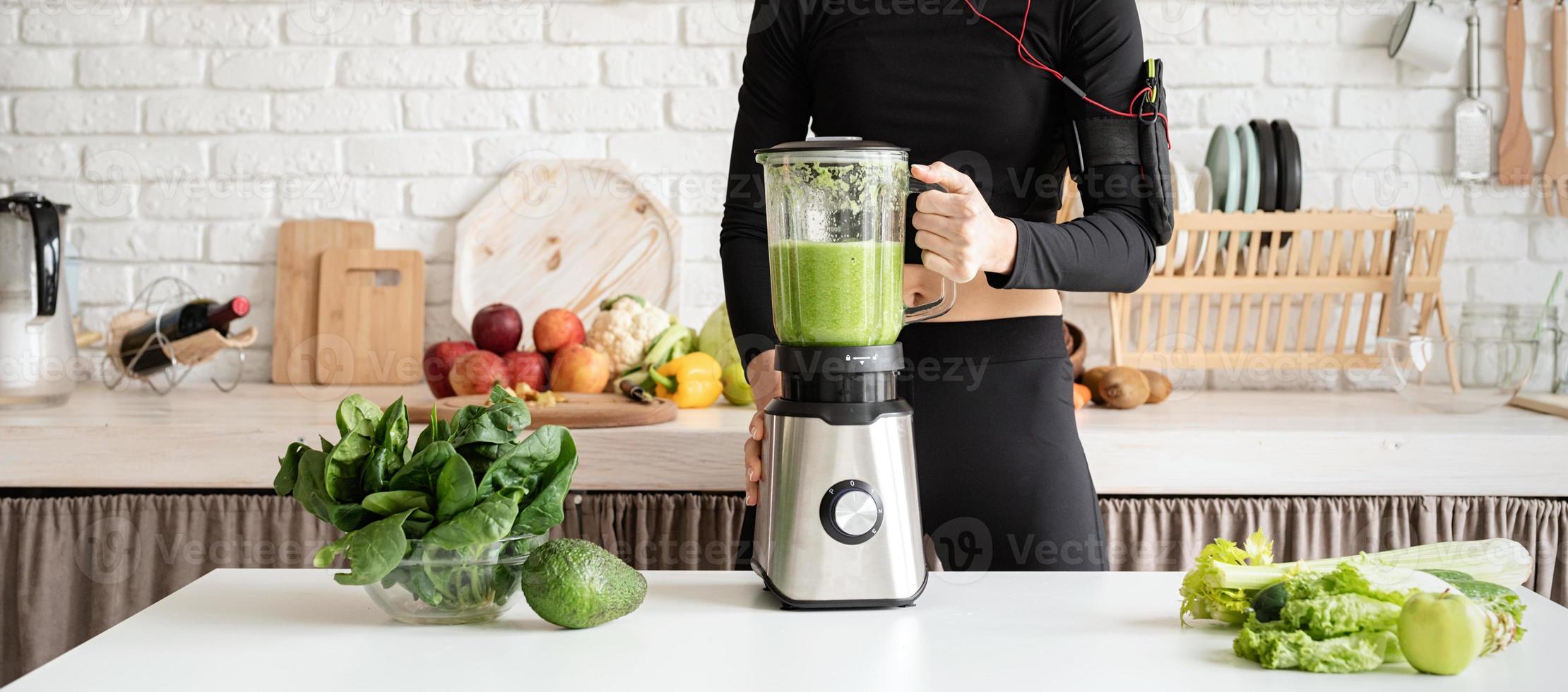 jovem loira sorridente fazendo suco verde na cozinha de casa foto