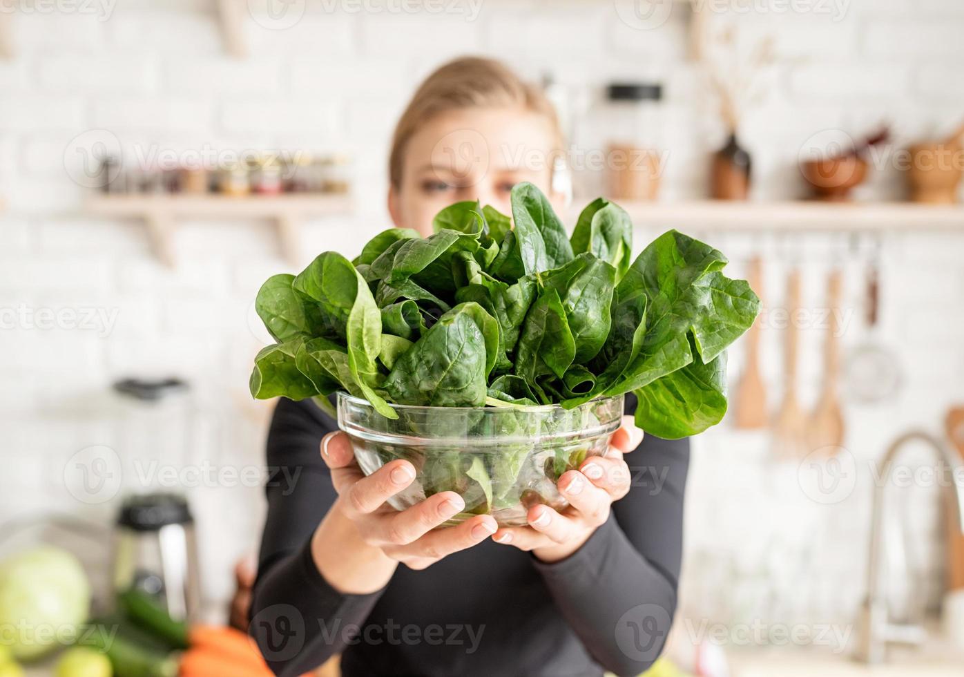 mulher segurando uma tigela de espinafre fresco na cozinha foto