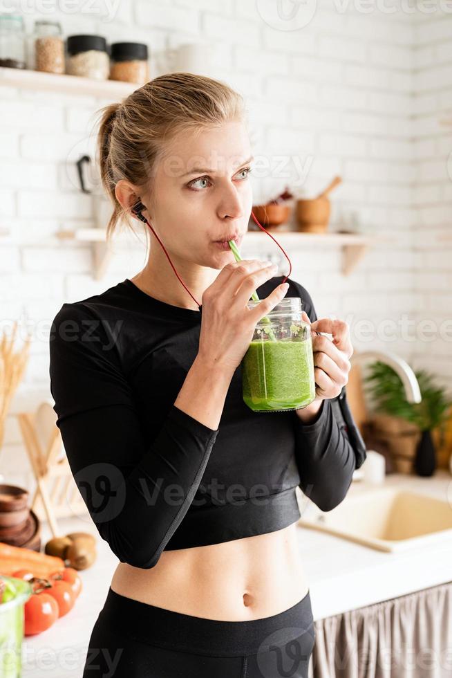 mulher bebendo smoothie verde do frasco de vidro na cozinha de casa foto