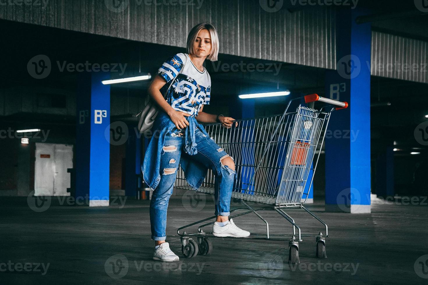 mulher vestida de jeans com carrinhos de compras no estacionamento foto