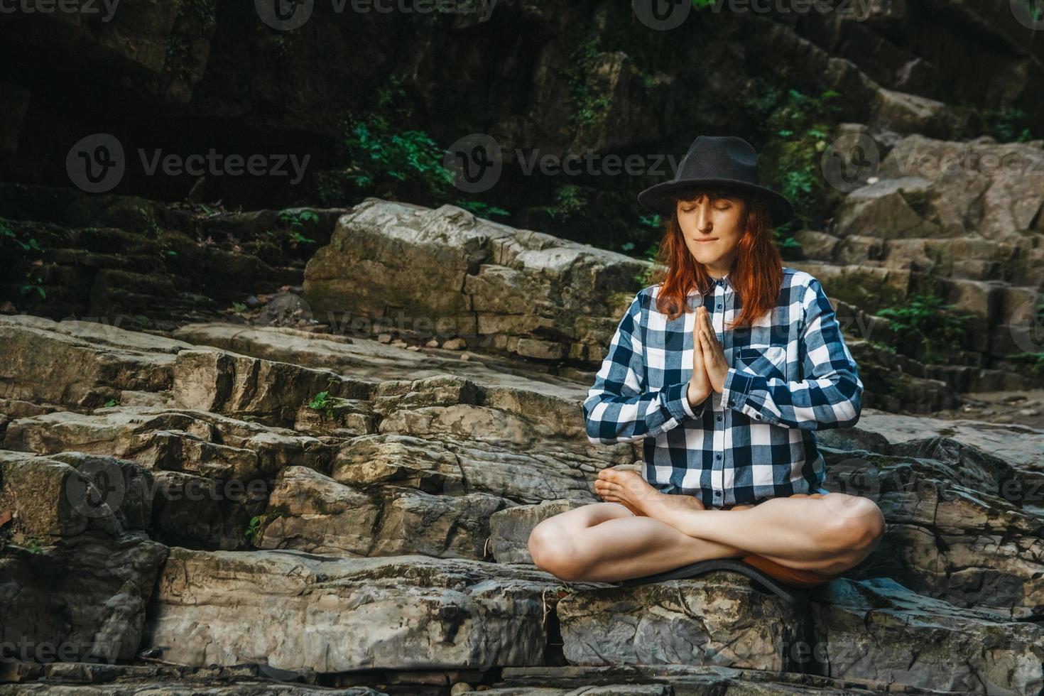 mulher de chapéu e camisa meditando sobre pedras em posição de lótus foto