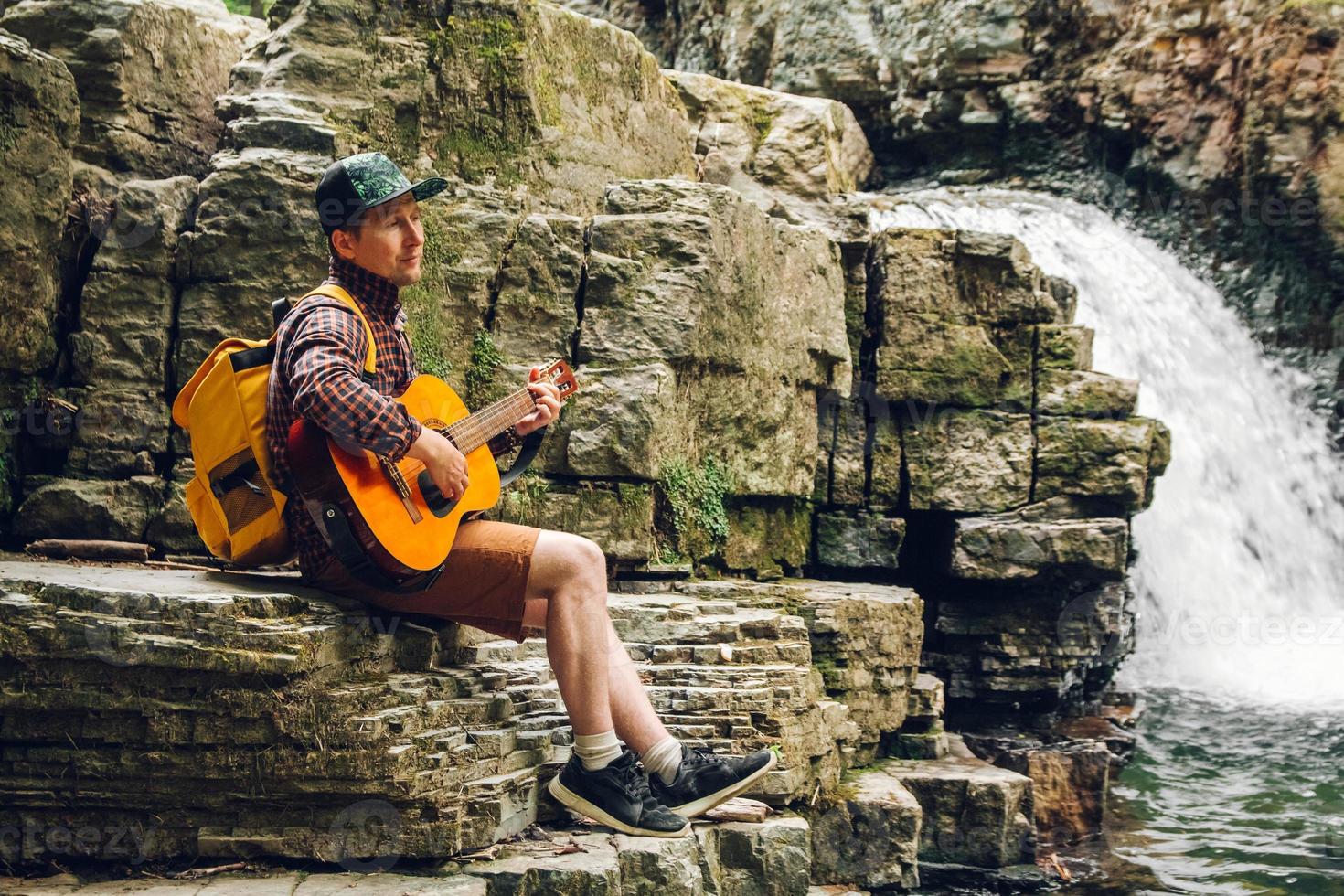 homem tocando violão sentado perto de uma cachoeira foto