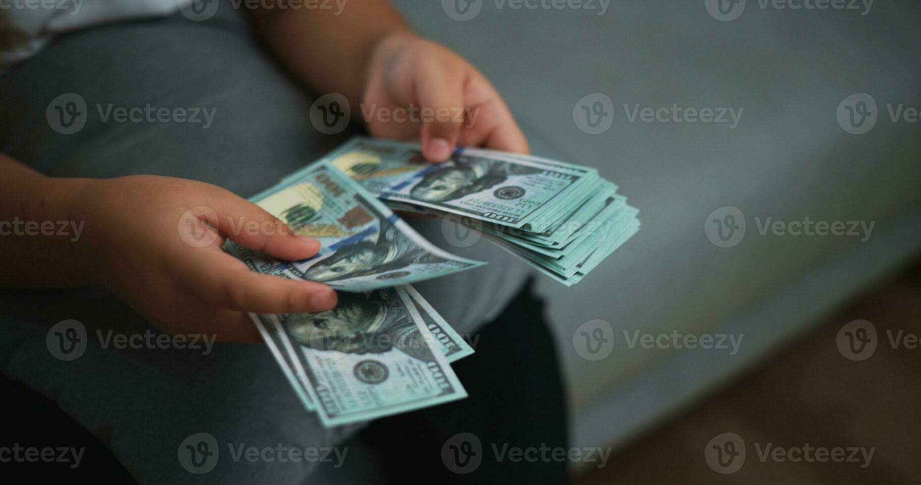 retrato fechar acima mãos do jovem ásia mulher apreciar contando dinheiro dólares notas em sofá dentro a vivo quarto às lar. foto
