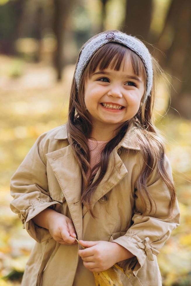 linda garotinha com um casaco bege caminhando no parque de outono foto