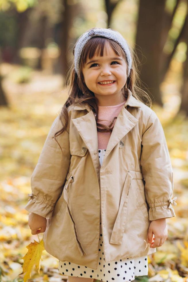menina feliz segurando uma folha de bordo amarela no parque outono foto
