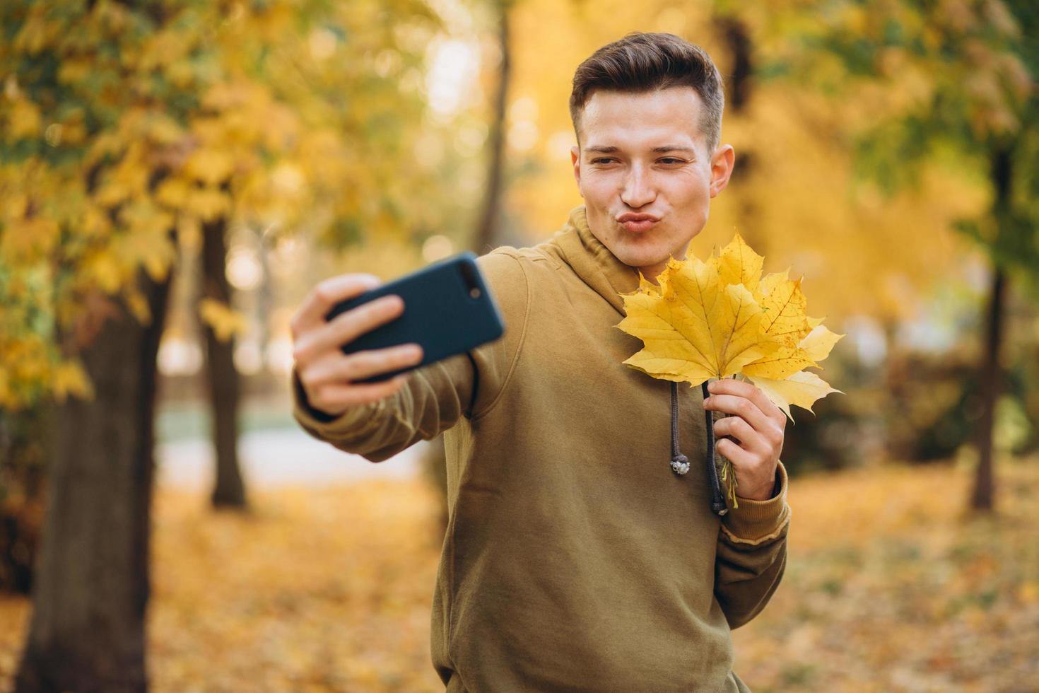 cara segurando um buquê de folhas e tirando uma selfie com um beijo no parque foto