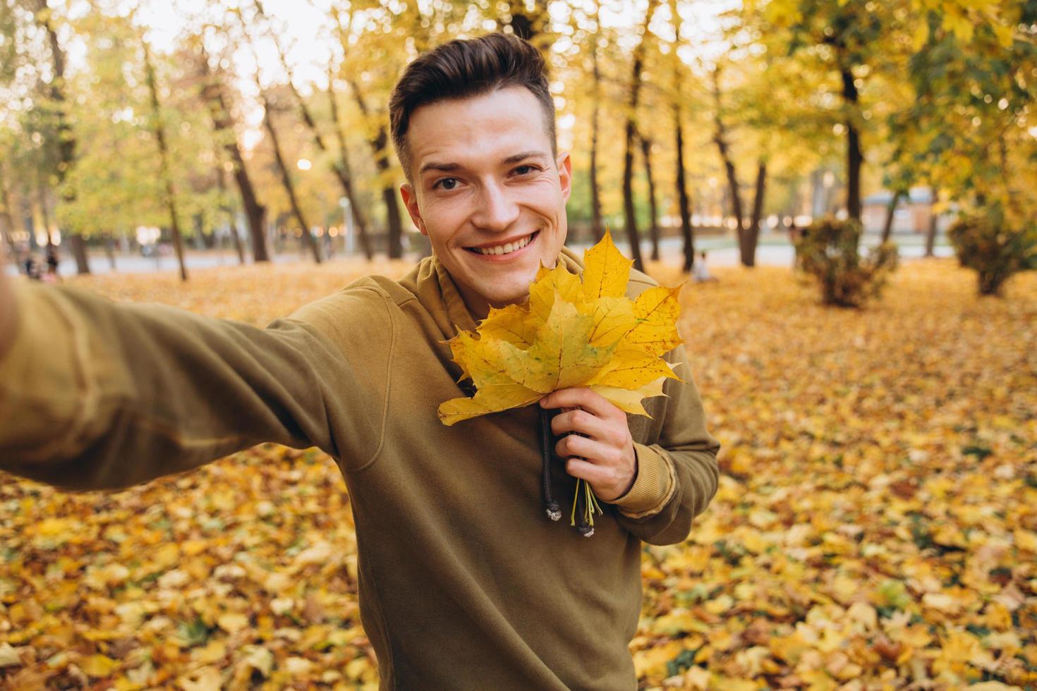 o cara segurando um buquê de folhas de outono e tirando uma selfie no parque foto