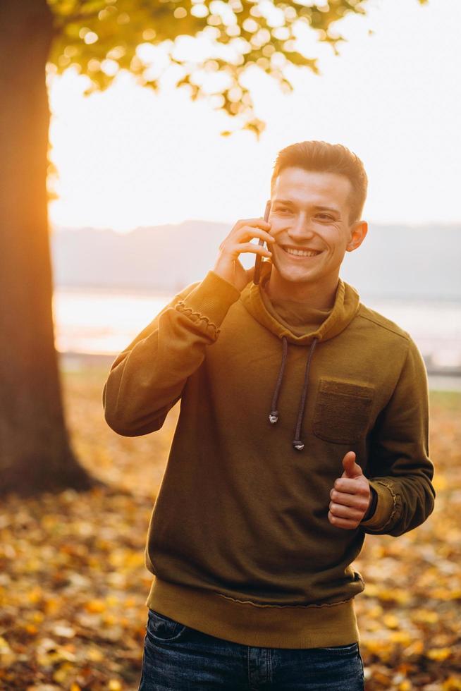 cara feliz sorrindo e falando ao telefone no parque de outono foto