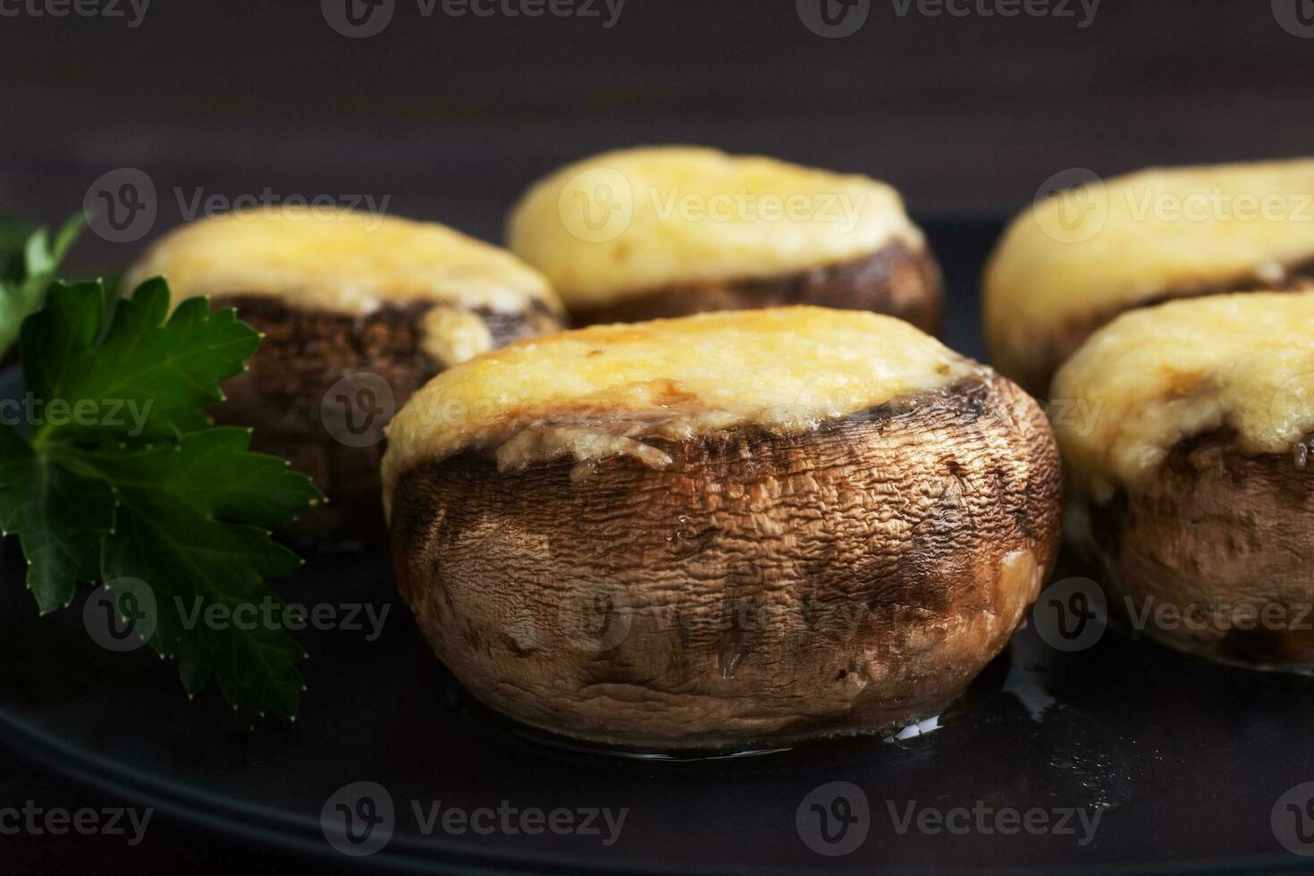 cogumelos assados recheados com queijo e ervas em um prato preto. fundo de madeira. foto