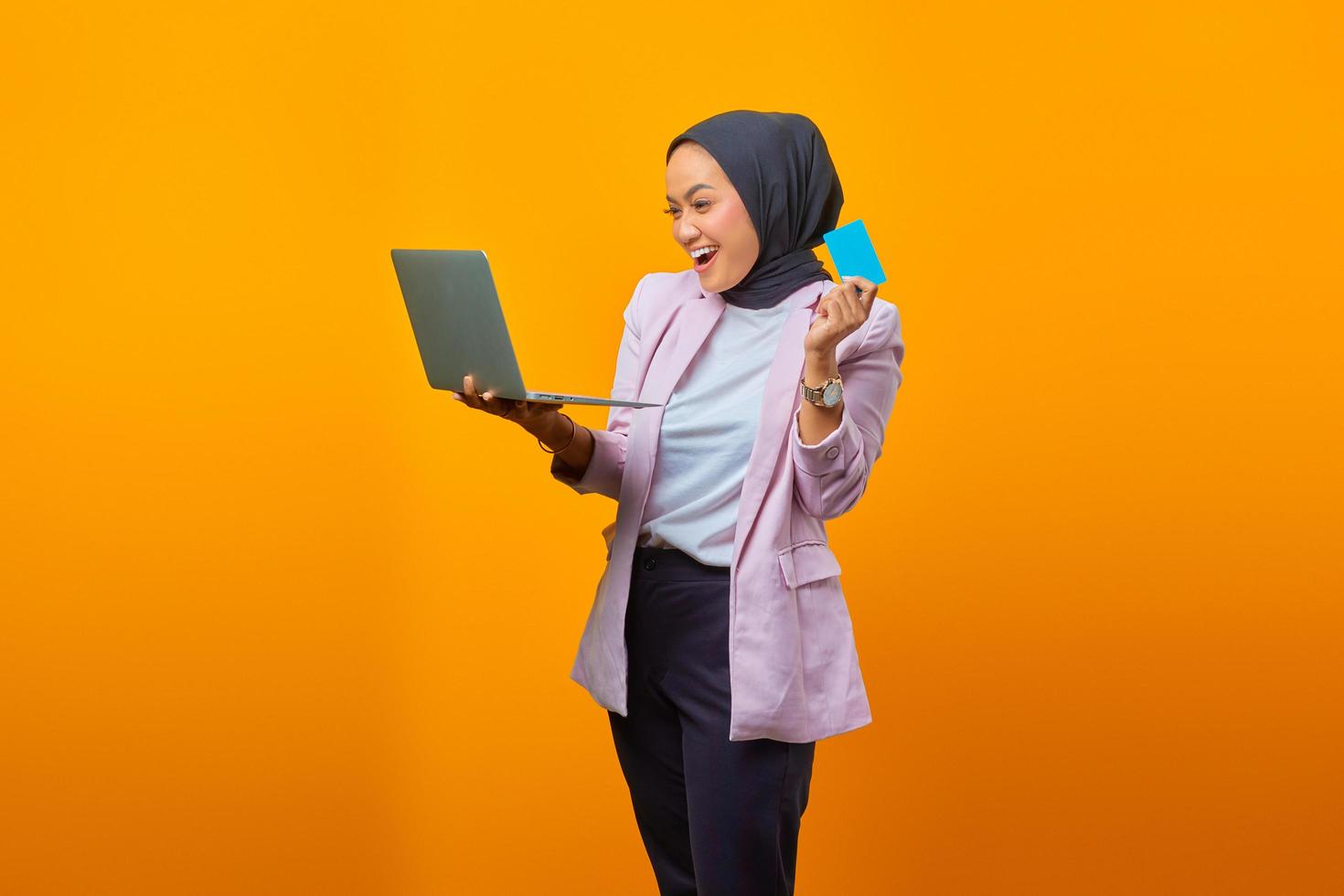 alegre mulher asiática segurando laptop e mostrando cartão de crédito foto