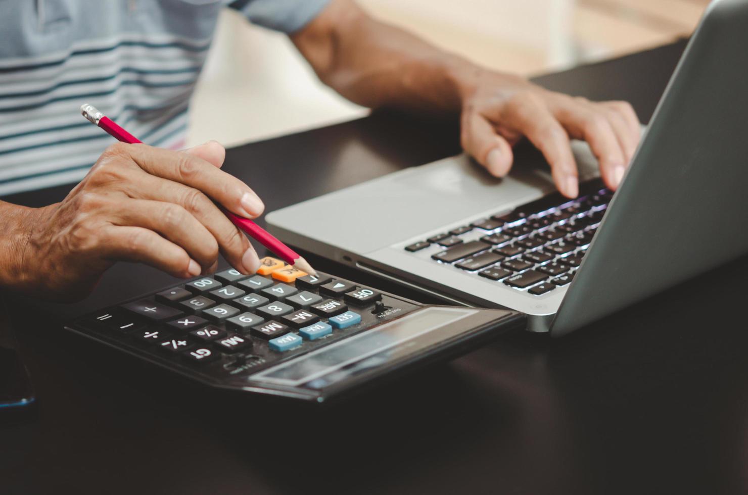 mão segurando um lápis, calculadora e teclado de computador na mesa. foto