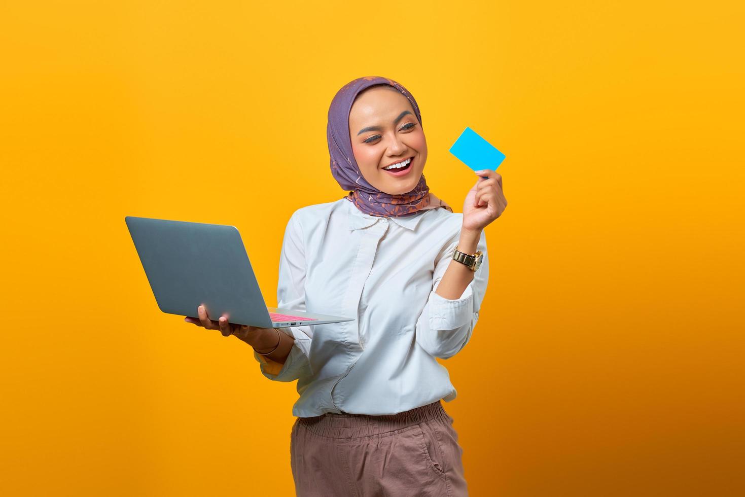 alegre mulher asiática segurando um laptop e olhando um cartão em branco foto