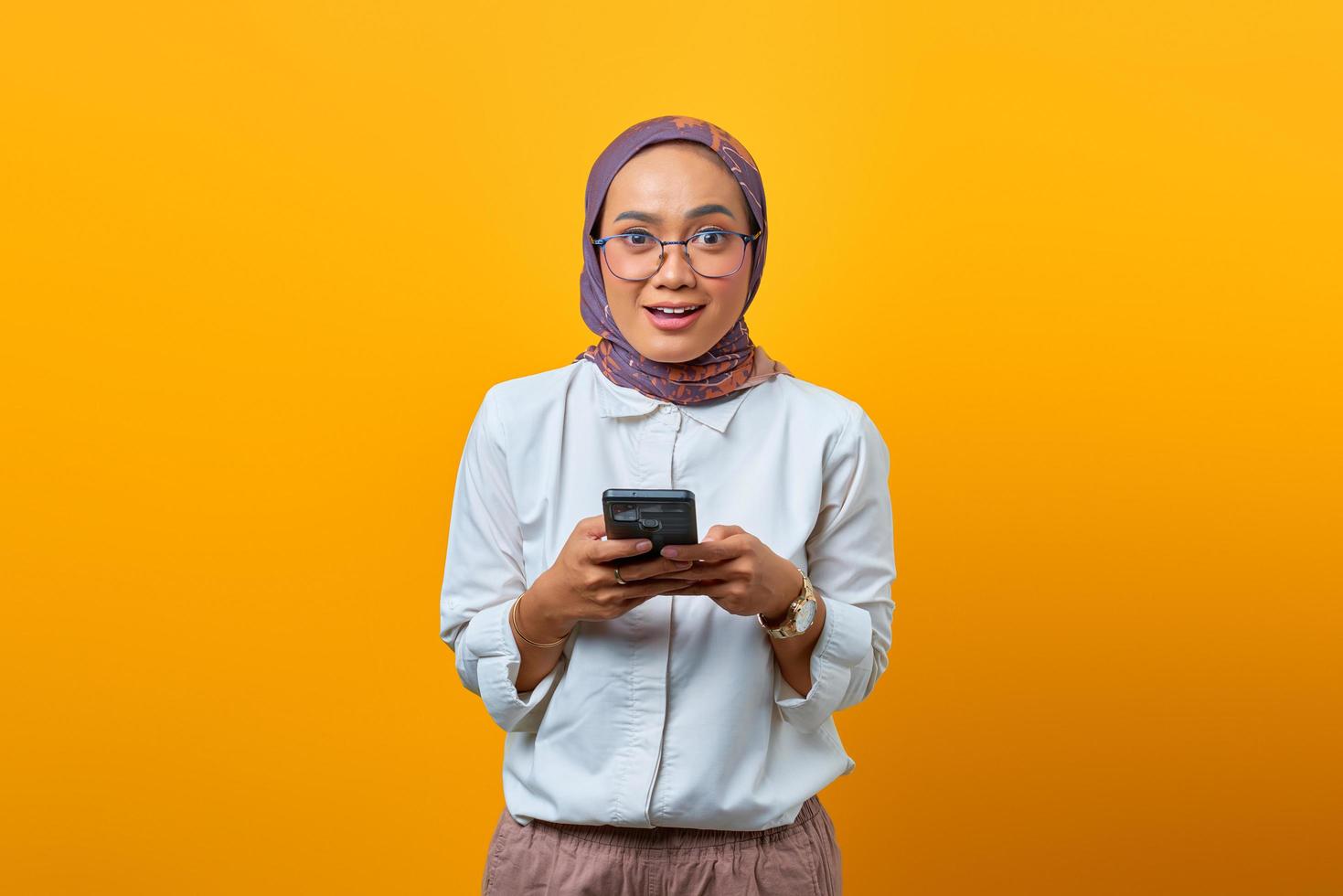 Mulher asiática chocada usando um telefone celular e olhando para a câmera foto