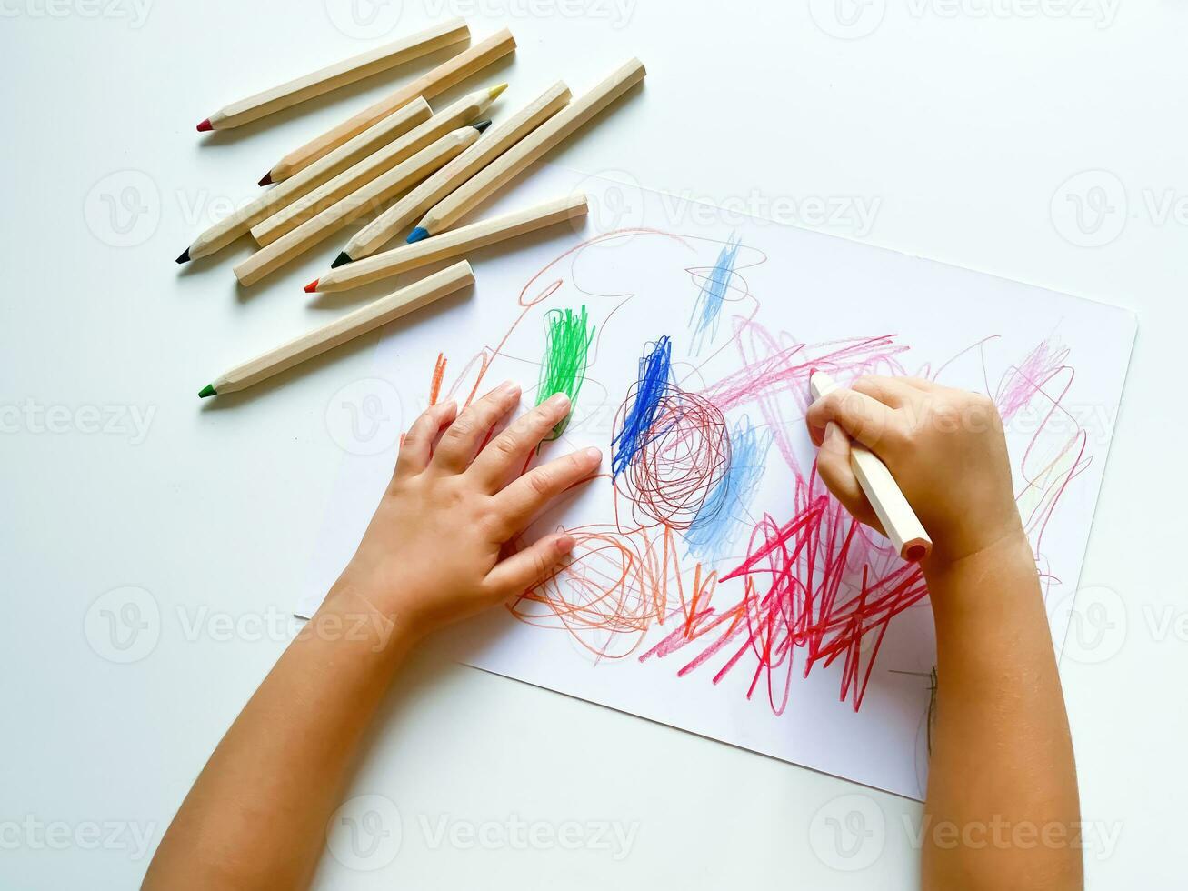 pequeno criança desenha com colori lápis em papel em branco mesa. foto