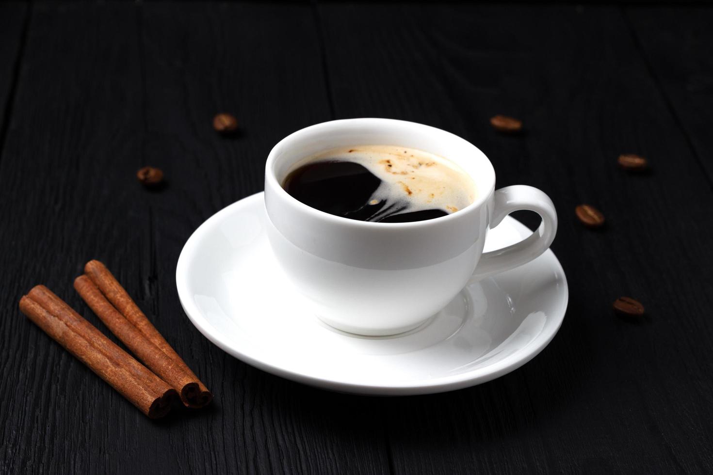 café preto em uma xícara branca com canela e espuma foto