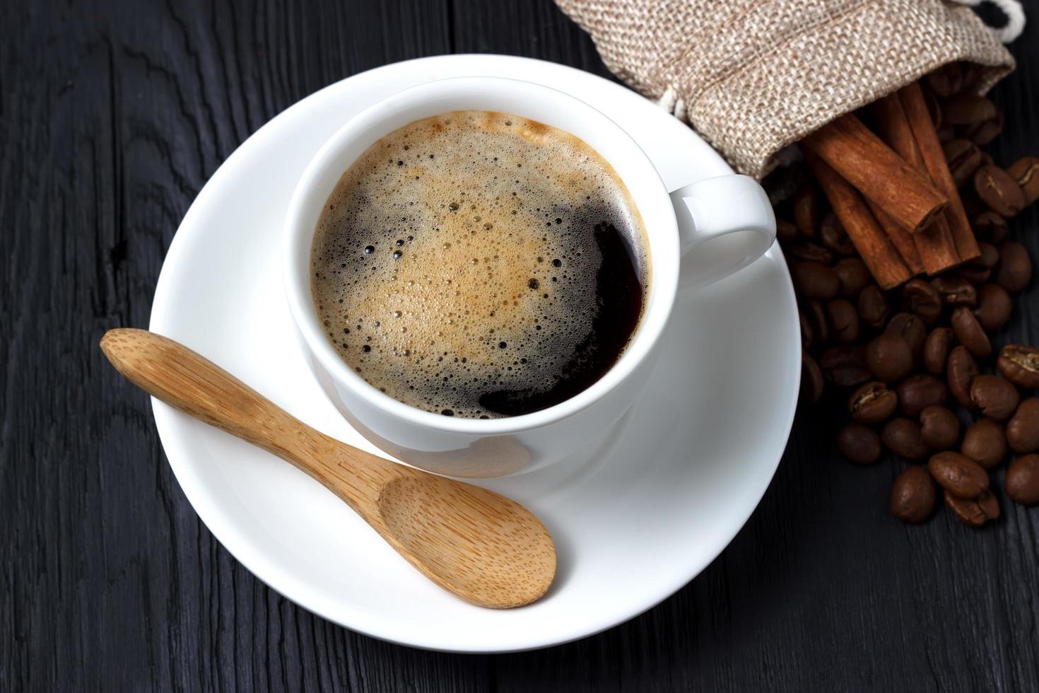 café quente com canela, uma colher de pau e um saco de grãos de café foto