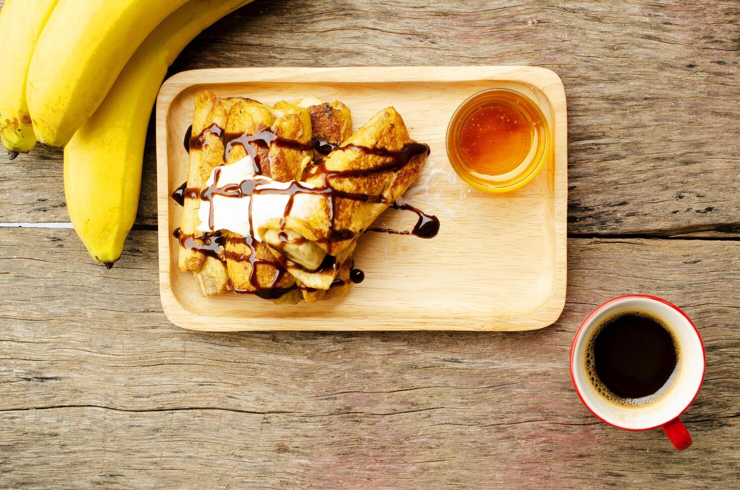 torrada francesa de banana com mel e café preto xícaras vermelhas na mesa de madeira foto