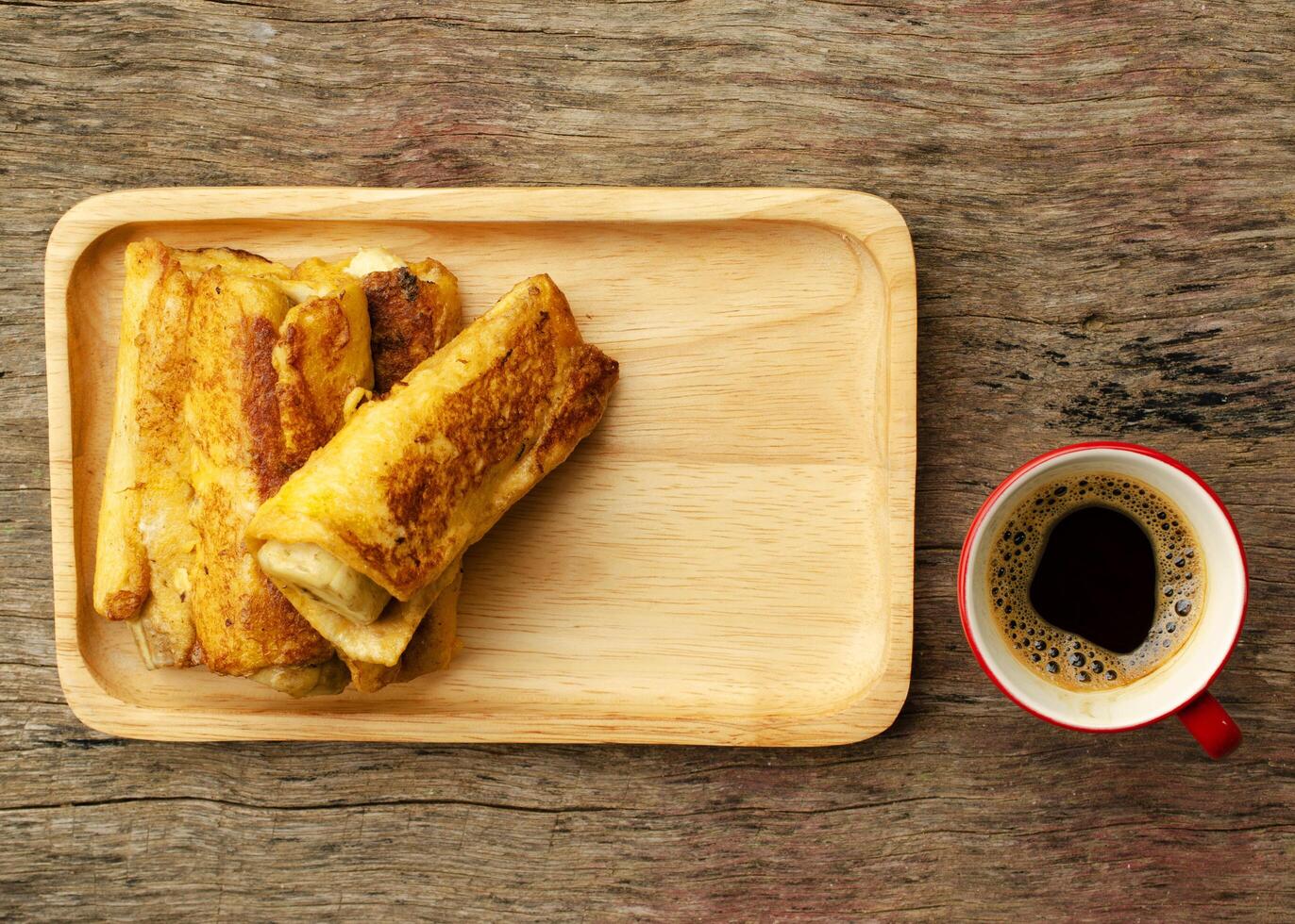 torrada francesa de banana com xícara de café vermelho no fundo da mesa de madeira foto