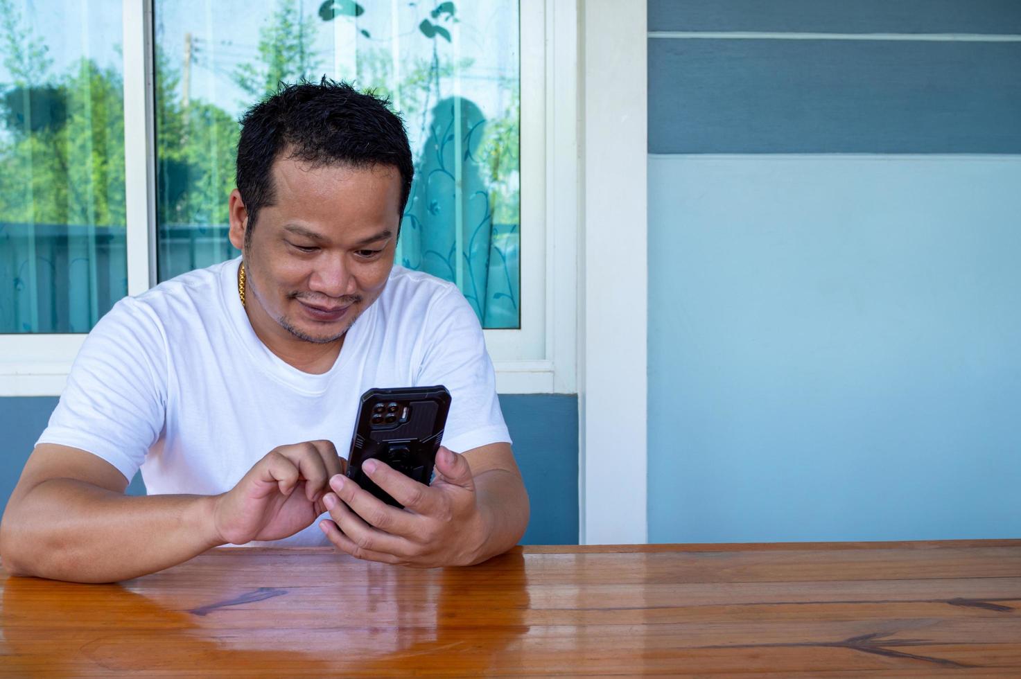 homem asiático vestindo camisa branca usando o telefone em uma mesa de madeira foto