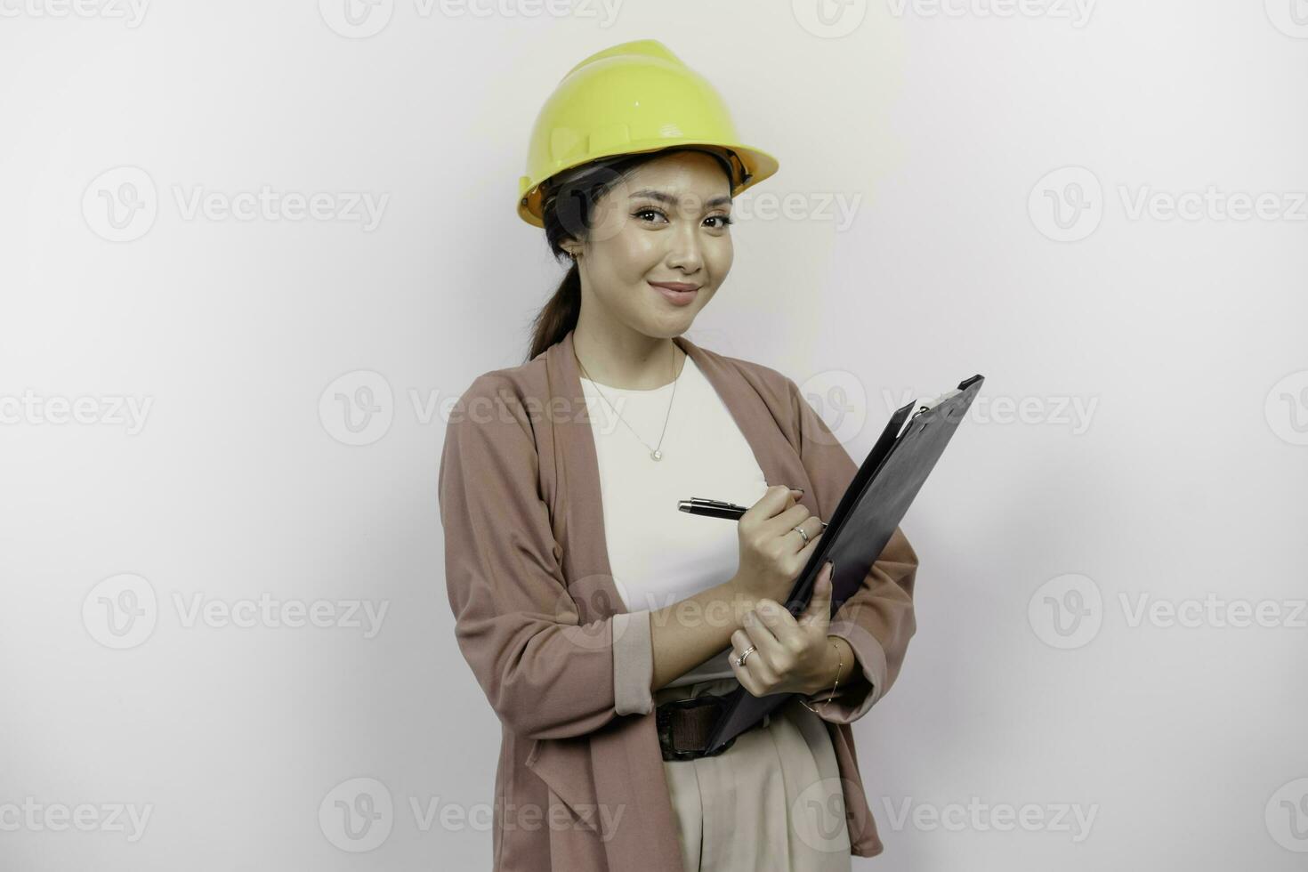 sorridente jovem ásia mulher empregado vestindo segurança capacete enquanto segurando uma prancheta, isolado de branco fundo foto